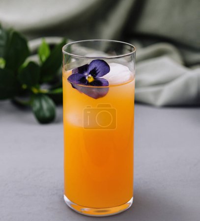 Chic glass of orange cocktail adorned with a pansy on a sophisticated table setting