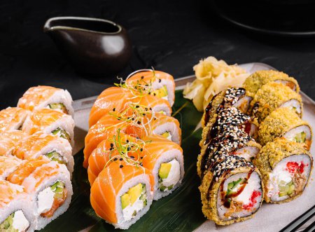 Elegante selección de sushi con rollos y sashimi en pizarra oscura con salsa de soja y palillos