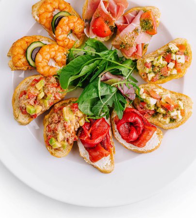 Top view of a variety of bruschetta with fresh ingredients on a round plate, isolated on white