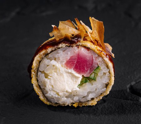 Gros plan d'un délicieux rouleau de sushi avec thon frais et garniture croustillante sur fond d'ardoise texturée