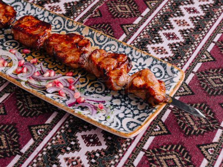 Delicious barbecued meat skewers served with onions on an ethnic-patterned plate over an intricate tablecloth