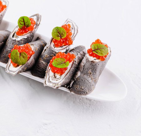 Elegante schwarze Crêpes mit Frischkäse gefüllt und mit rotem Kaviar und frischen Kräutern belegt