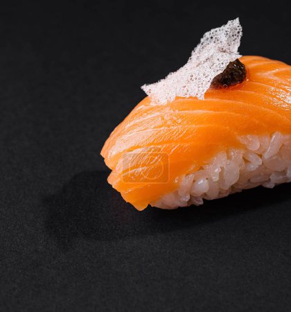 Zbliżenie smakowitego sushi z łososia nigiri ozdobionego delikatnym dodatkiem, wyizolowanego na ciemnym tle
