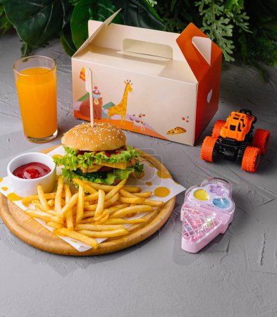 Cheerful children's meal with burger, fries, and orange juice next to a toy car and phone