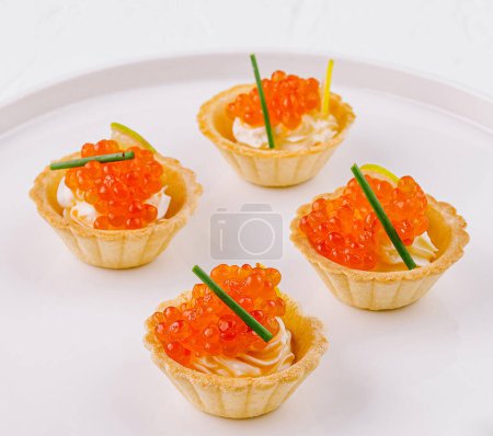 Gourmet mini tartlets filled with cream cheese and topped with salmon roe, served on a modern plate
