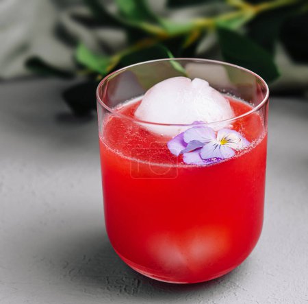 Elegant watermelon cocktail adorned with an ice sphere and delicate pansy, perfect for summer refreshment
