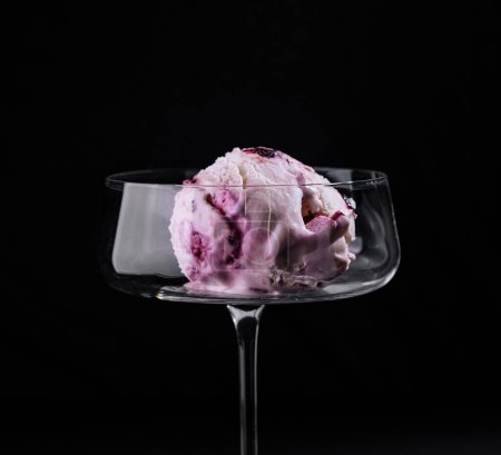 Indulge in a single scoop of berry ice cream presented in a sophisticated stem glass against a dark backdrop