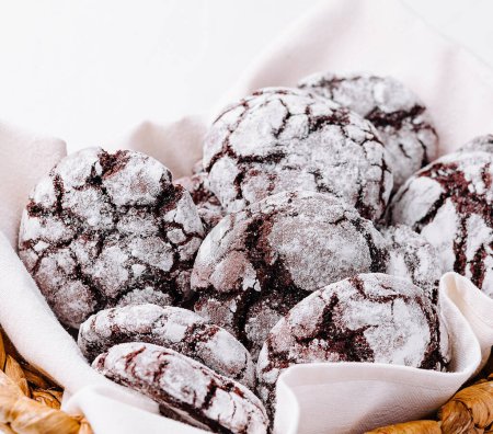 Basket of freshly baked chocolate crinkle cookies dusted with powdered sugar on a white background