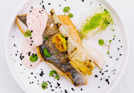 Présentation élégante d'un filet de poisson poêlé avec sauce rose, herbes et fleurs comestibles sur une assiette blanche