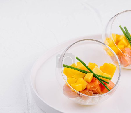 Elegant presentation of salmon and mango tartare with chive garnish in modern glass dishes on a white backdrop