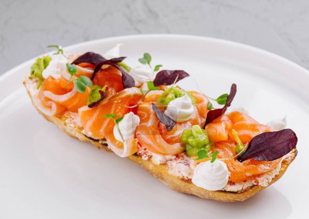 Elegant smoked salmon bruschetta garnished with herbs and cream cheese, presented on a clean white dish