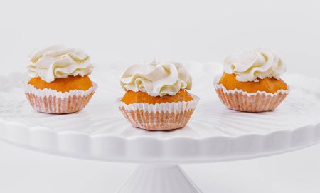 Drei leckere Cupcakes mit cremigem Belag auf einem klassischen weißen Kuchenständer vor weißem Hintergrund