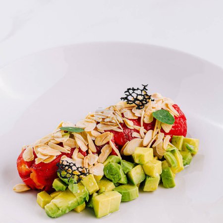 Fresh avocado salad with bell pepper and nuts and slivered almonds on a white plate