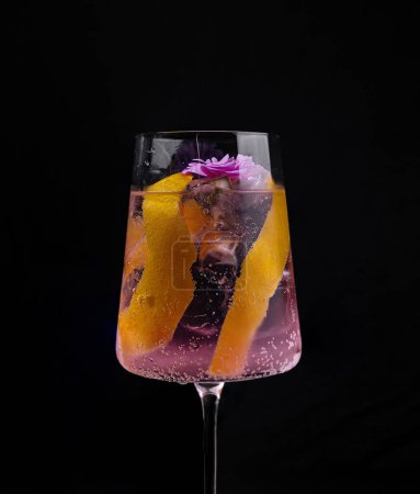Stilvoller Gin Tonic Cocktail mit einer Blume und Zitrusschalen vor dunklem Hintergrund