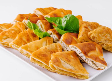 Selection of golden puff pastries served with basil garnish on a white background
