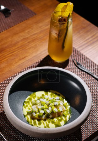 Wunderschön präsentierte Gourmet-Mahlzeit mit einem erfrischenden Cocktail an einem dunklen, stilvollen Restauranttisch