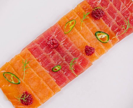 Top view of plate of salmon carpaccio garnished with lime and jalapeo slices on a white table