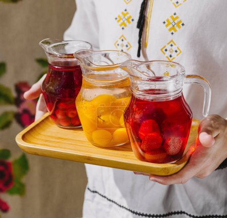Person presents three pitchers of refreshing fruit-infused water on a wooden tray close up