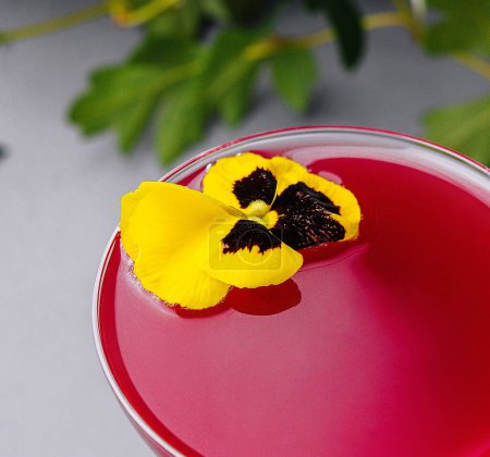 Vibrant pink drink in a coupe glass, adorned with a delicate edible pansy, symbolizing sophistication