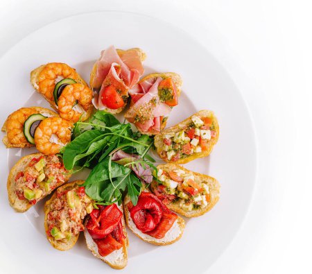 Top view of a variety of bruschetta with fresh ingredients on a round plate, isolated on white
