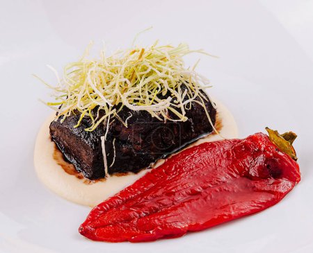 Elegant dish of tender braised beef on a smear of puree with a vibrant red vegetable garnish on a white plate