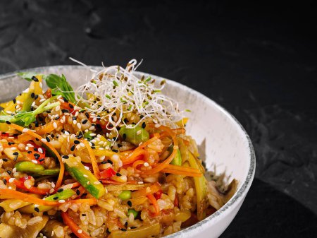 Vibrant rice bowl with fresh vegetables and sesame, served in a stylish dish on a dark background