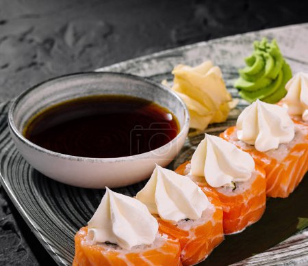 Eleganckie bułki sushi z dodatkiem sera śmietankowego, podawane z sosem sojowym, wasabi i imbirem na szykownym talerzu