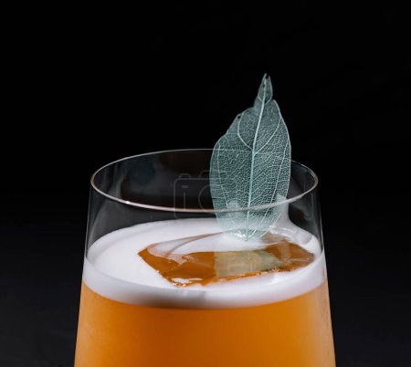 Moderner Cocktail mit schaumigem Oberteil und zarter Blattgarnitur, präsentiert vor dunklem Hintergrund