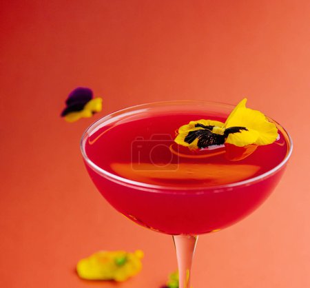 Vibrant cocktail decorated with edible flowers, presented in a stemmed glass against a warm-toned backdrop