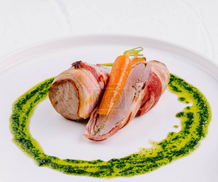Elegant pork tenderloin wrapped in bacon, served with carrot and a vibrant pesto drizzle