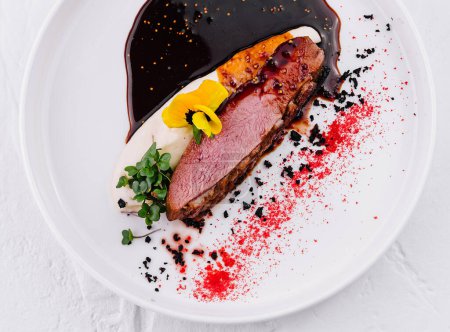 Elegantly presented duck breast with puree, berry sauce, and edible flowers on a white plate
