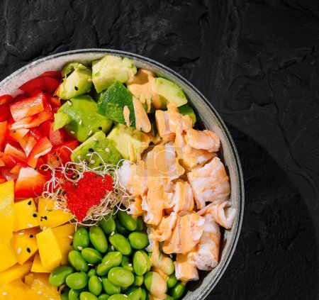 Colorful bowl of salad with shrimps, avocado, mango, and edamame on a dark background