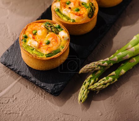 Gourmet mini quiches with fresh asparagus on a slate plate close up