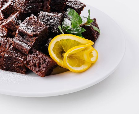 Plate of freshly baked chocolate brownie cubes, dusted with powdered sugar, garnished with lemon and mint