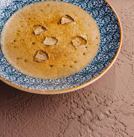 Elegant bowl of smooth, blended soup garnished with truffle slices, on textured background