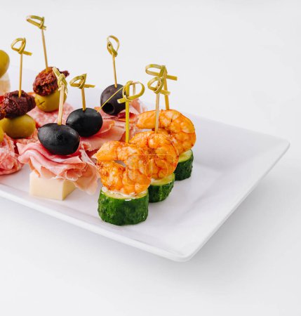 Exquisite gourmet finger food appetizer platter with an elegant assortment of cheese. Shrimp. Olives. Salami. Cucumber. Grape. And sundried tomato. Perfect for catering. Parties. And banquets