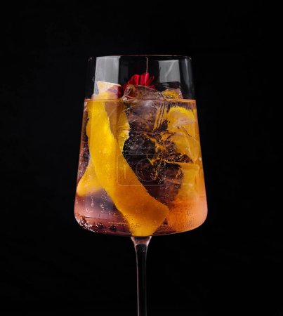 Hohes Glas mit Zitronenschale, gefüllt mit einem sprudelnden, bernsteinfarbenen Getränk, begleitet von einer geschlossenen Flasche