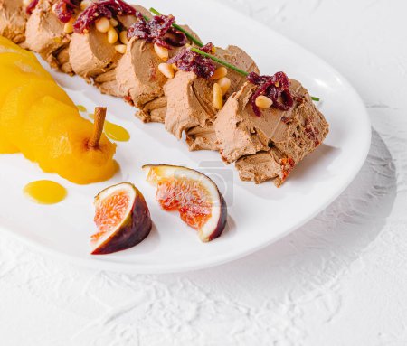 Delicately sliced pork pate adorned with figs and a smooth pear puree on a white plate
