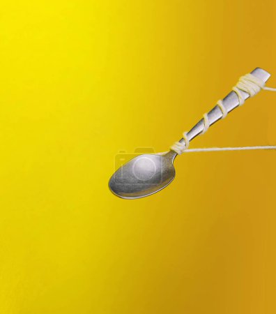 Silver spoon tied with string against a vibrant yellow backdrop, creating an illusion of floating