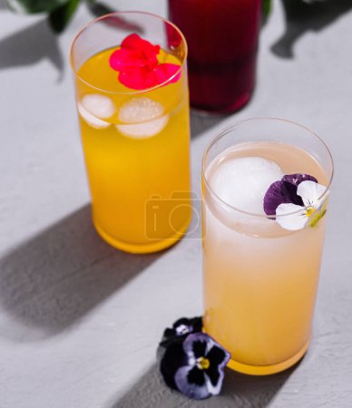 Two colorful cocktails adorned with edible flowers on a bright, sunny day