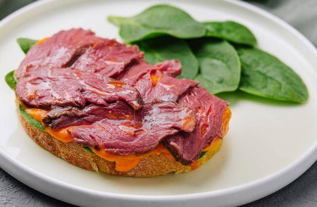 Elegant dish of sliced beef tenderloin atop a toasted bread slice and fresh spinach, presented with silverware