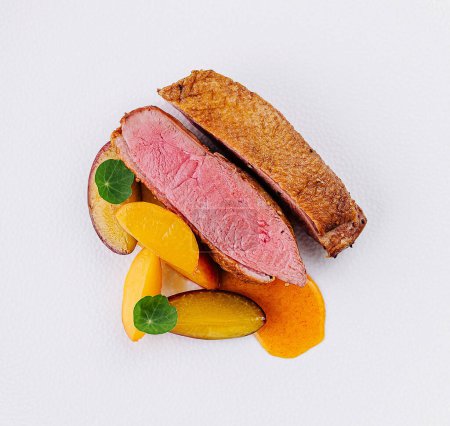 Elegant dish of sliced duck breast with fresh peach pieces, styled delicately on a round, white porcelain plate