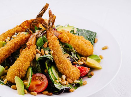 Appetizing plate of breaded shrimp on a bed of greens with avocado, tomato, and pine nuts