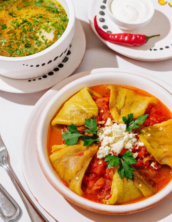 Vibrant bowl of spicy soup served with stuffed peppers, garnished with fresh herbs and cheese