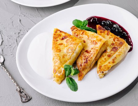 Delicious crepes with berry syrup accompanied by cheese pancakes top view