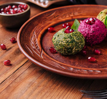 Trio of green, pink, and traditional falafel on rustic plate adorned with pomegranate