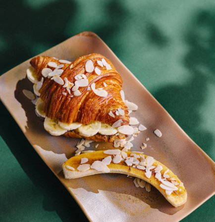 Elegante croissant de almendras con rodajas de plátano servidas en un elegante plato bajo una suave iluminación
