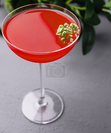 Vibrant red cocktail in a stemmed glass, adorned with white flowers, presented on a sleek surface