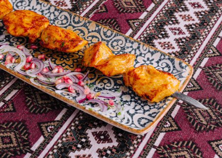 Brochettes de poulet grillées juteuses servies sur une assiette décorative avec des oignons, sur un textile à motifs
