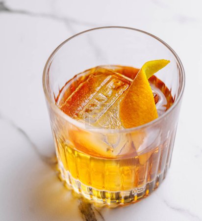 Close-up of a classic old fashioned cocktail garnished with a fresh orange twist on a marble surface